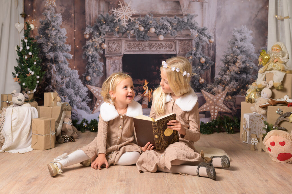 deux petites filles lisent un livre au coin du feu dans un décor de Noël pour seance photo au Grau du roi